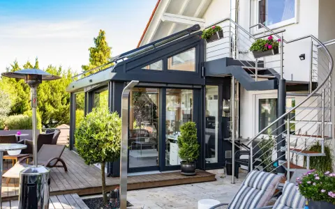 Moderner Wintergarten mit Außentreppe und Terrassenmöbeln. Ein Heizpilz sorgt für Wärme.