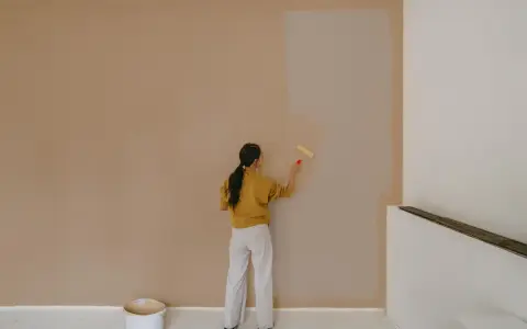 Frau streicht Wand neu. Man fragt sich, wie lange braucht wandfarbe zum trocknen, während sie die helle Farbe aufträgt.