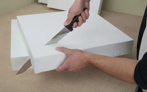 Hände schneiden mit einem Messer präzise Styropor für ein Bastelprojekt.