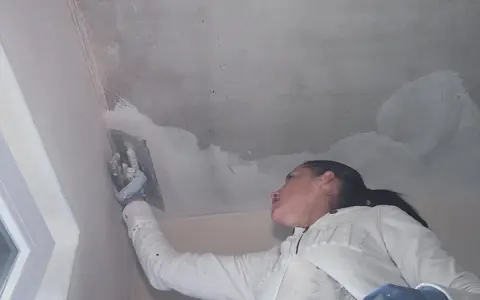 Frau verputzt die Decke mit einer Kelle.