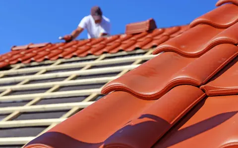 Dachdecker verlegt rote Ziegel. Die Frage "wie lange halten dachziegel" wird durch die Langlebigkeit des Materials beantwortet.