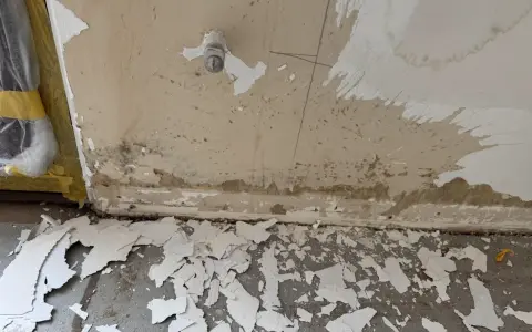 Vorbereitung zum zumauern einer Heizungsnische: abgeplatzter Putz und Schmutz am Boden, Wand mit Wasserflecken und einem Ventil.