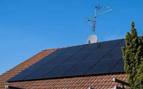 Dach mit Ziegeln, darauf schwarze Solarmodule für HEMS Photovoltaik. Eine Satellitenschüssel und Antenne sind ebenfalls zu sehen.