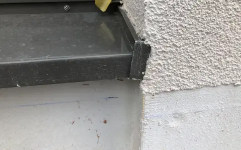 Detailaufnahme einer Fensterbank, die mit Klebeband provisorisch abgedichtet ist. Die raue Fassade und die graue Fensterbank sind gut erkennbar.