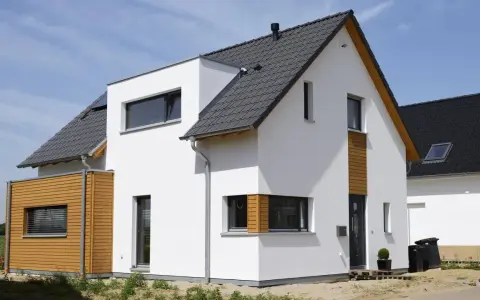 Moderner Neubau trocknet im Sonnenschein. Weiße Fassade, Holzverkleidung und dunkles Dach.