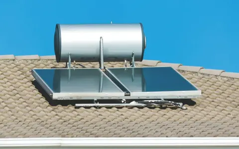 Ein pvt kollektor mit einem Warmwasserspeicher auf einem Ziegeldach unter blauem Himmel.