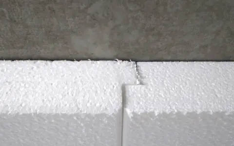Detailaufnahme: Styrodur kleben an einer Betonwand. Die weißen Styroporplatten sind präzise zugeschnitten und stoßen nahtlos aneinander.