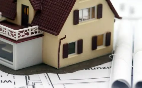 Modell eines Einfamilienhauses auf Bauplänen, daneben zwei aufgerollte Pläne. Ein Baukasten-BHKW könnte hier integriert werden.