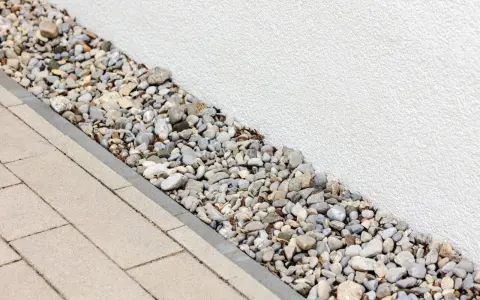 Kiesbett als Spritzschutz am Haus, neben gepflastertem Weg.