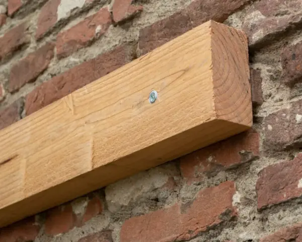 Ein Holzbalken wird mit einer Schraube an einer Ziegelwand befestigt.