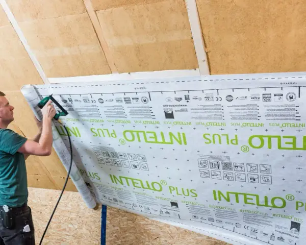 Mann bringt mit einem Tacker eine Dampfbremse an der Dachschräge an. Die Folie ist mit "INTELLO PLUS" bedruckt.