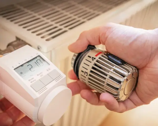 Hände tauschen ein sehr altes Thermostat gegen ein modernes Gerät an einem Heizkörper.