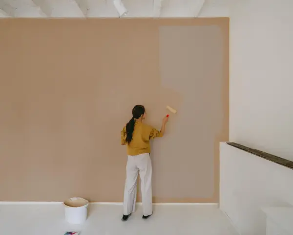 Frau streicht Wand neu. Man fragt sich, wie lange braucht wandfarbe zum trocknen, während sie die helle Farbe aufträgt.