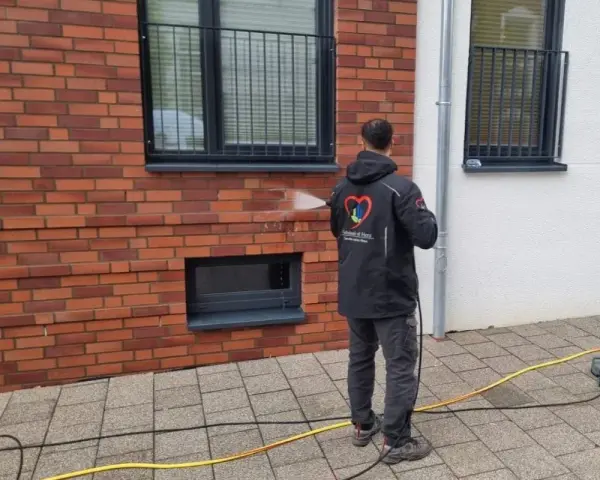 Mann reinigt mit Hochdruckreiniger die Ziegel-Fassade.