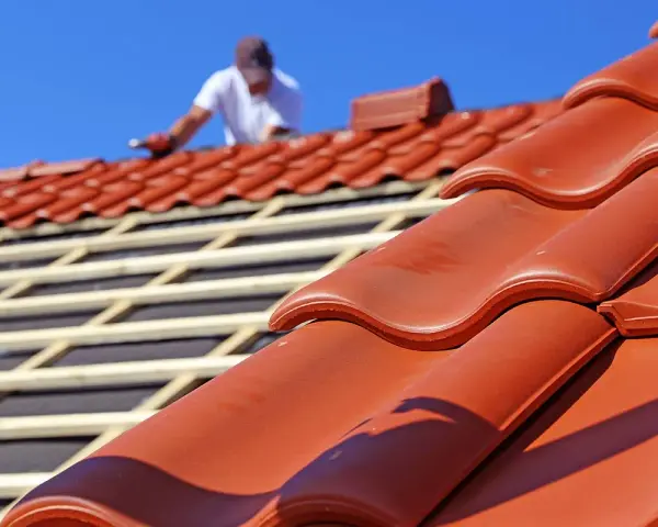 Dachdecker verlegt rote Ziegel. Die Frage "wie lange halten dachziegel" wird durch die Langlebigkeit des Materials beantwortet.