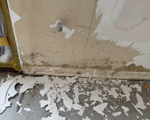 Vorbereitung zum zumauern einer Heizungsnische: abgeplatzter Putz und Schmutz am Boden, Wand mit Wasserflecken und einem Ventil.