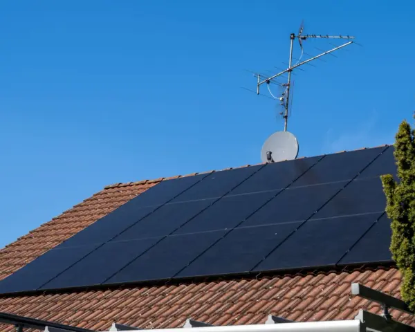 Dach mit Ziegeln, darauf schwarze Solarmodule für HEMS Photovoltaik. Eine Satellitenschüssel und Antenne sind ebenfalls zu sehen.