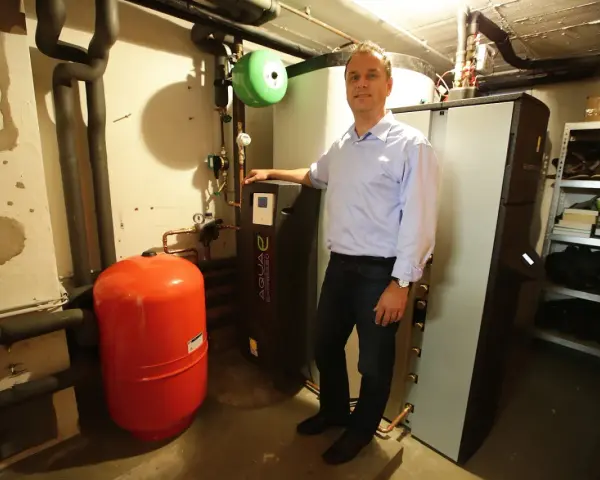 Mann steht neben Heizungsanlage, um Solarthermie zu optimieren. Roter Ausdehnungsbehälter und schwarze Wärmepumpe sichtbar.