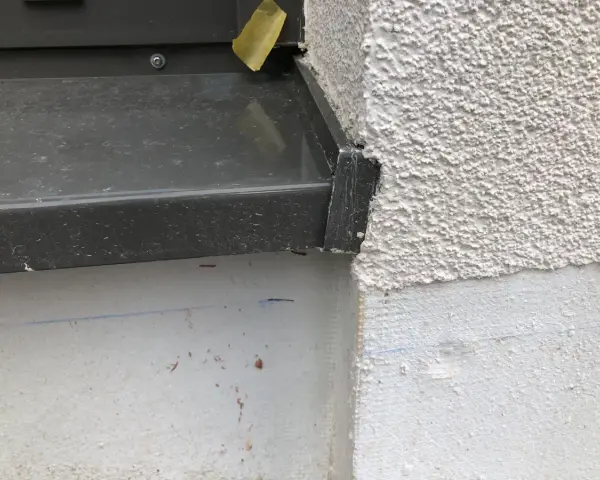 Detailaufnahme einer Fensterbank, die mit Klebeband provisorisch abgedichtet ist. Die raue Fassade und die graue Fensterbank sind gut erkennbar.