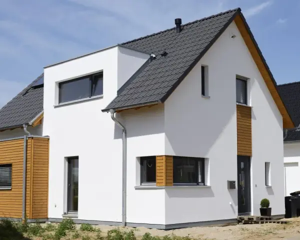 Moderner Neubau trocknet im Sonnenschein. Weiße Fassade, Holzverkleidung und dunkles Dach.
