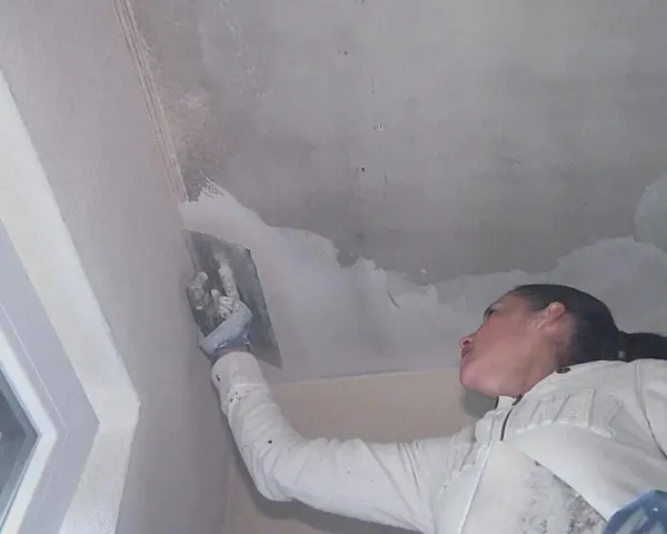 Frau spachtelt mit einem Werkzeug die Betondecke, um sie für die weitere Bearbeitung vorzubereiten.