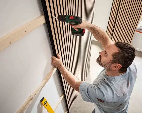 Mann montiert Akustikpaneele an Wand. Tolle Ideen für moderne Raumgestaltung und Schallschutz.