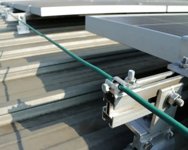 Detailaufnahme der Erdung einer PV-Anlage. Ein grünes Kabel wird sicher mit einer Klemme an der Aluminiumkonstruktion befestigt, die die Solarmodule auf dem Dach hält.