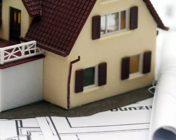 Modell eines Einfamilienhauses auf Bauplänen, daneben zwei aufgerollte Pläne. Ein Baukasten-BHKW könnte hier integriert werden.