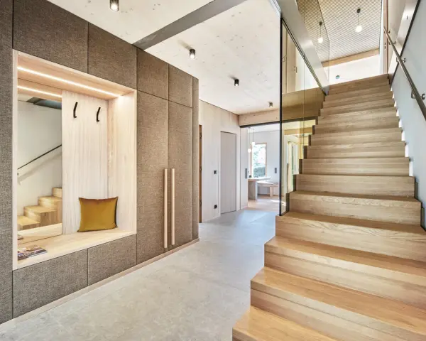 Moderne Diele mit Sitzbank und Garderobe, die Treppe aus verschiedenen **Hartholzarten** strahlt Wärme aus.