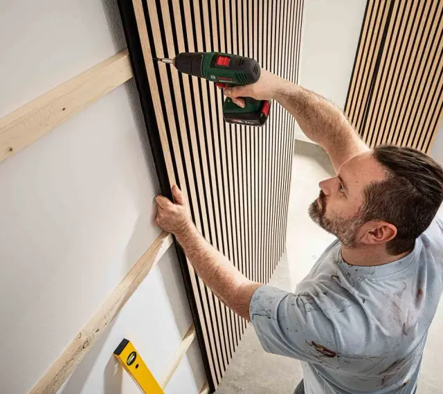 Mann montiert Akustikpaneele an Wand. Tolle Ideen für moderne Raumgestaltung und Schallschutz.