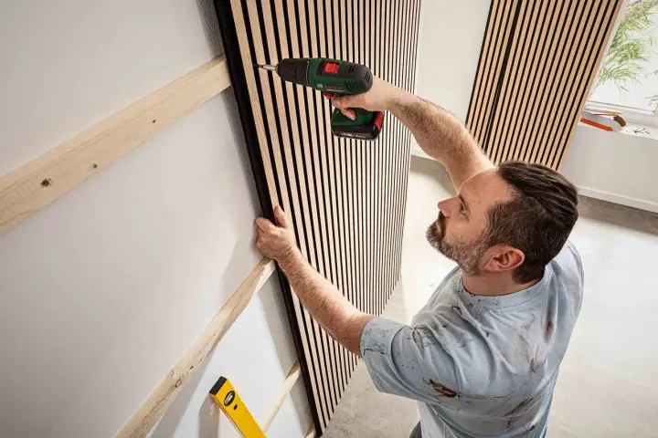 Mann montiert Akustikpaneele an Wand. Tolle Ideen für moderne Raumgestaltung und Schallschutz.