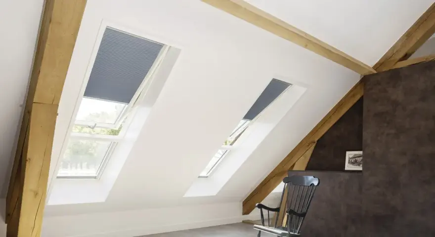 Schicke Dachfenster mit Plissees verkleiden. Holzbalken und ein gemütlicher Schaukelstuhl schaffen eine warme Atmosphäre.
