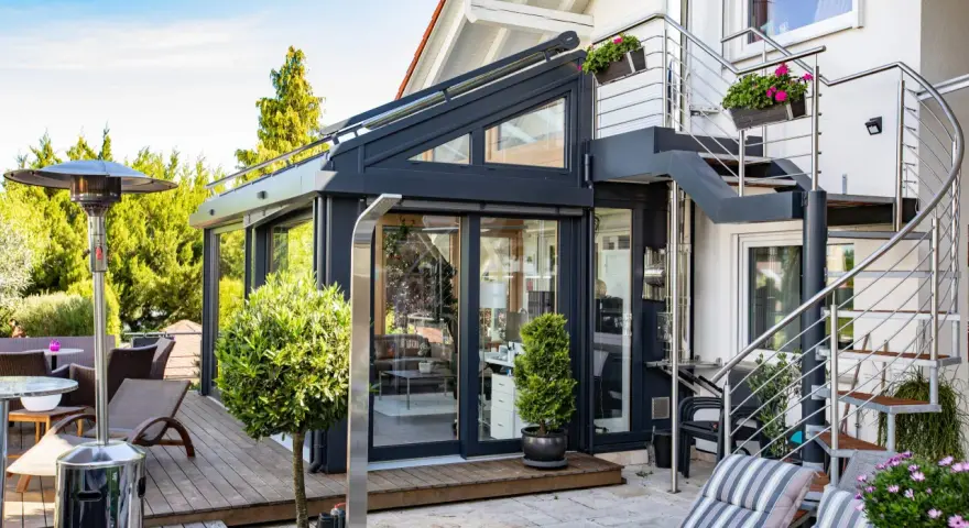 Moderner Wintergarten mit Außentreppe und Terrassenmöbeln. Ein Heizpilz sorgt für Wärme.