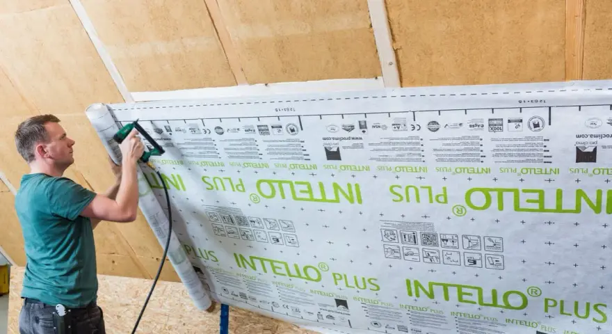 Mann bringt mit einem Tacker eine Dampfbremse an der Dachschräge an. Die Folie ist mit "INTELLO PLUS" bedruckt.