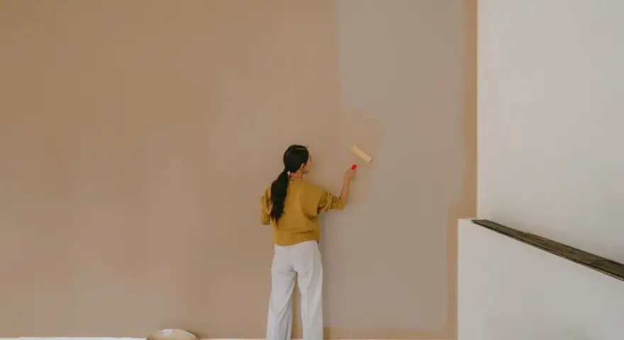 Frau streicht Wand neu. Man fragt sich, wie lange braucht wandfarbe zum trocknen, während sie die helle Farbe aufträgt.