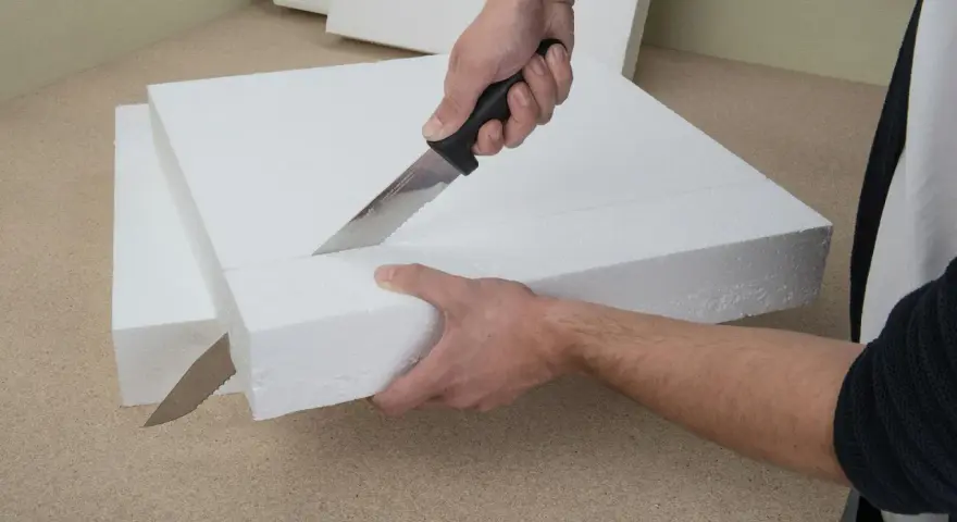 Hände schneiden mit einem Messer präzise Styropor für ein Bastelprojekt.