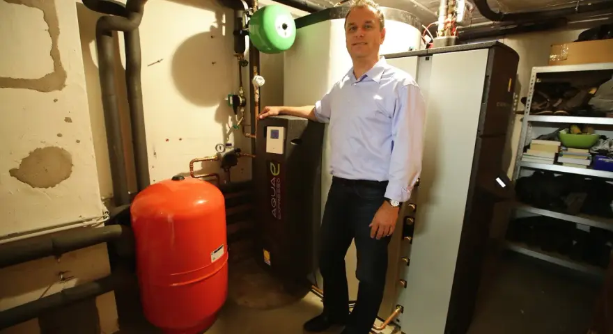 Mann steht neben Heizungsanlage, um Solarthermie zu optimieren. Roter Ausdehnungsbehälter und schwarze Wärmepumpe sichtbar.
