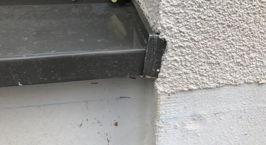 Detailaufnahme einer Fensterbank, die mit Klebeband provisorisch abgedichtet ist. Die raue Fassade und die graue Fensterbank sind gut erkennbar.