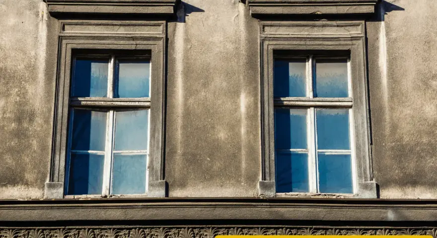 Zwei alte Fenster mit blauen Scheiben an einer verwitterten Fassade. Eine energetische Sanierung der Fenster würde sich hier lohnen.