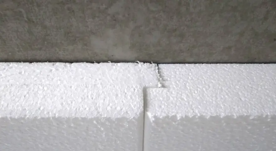 Detailaufnahme: Styrodur kleben an einer Betonwand. Die weißen Styroporplatten sind präzise zugeschnitten und stoßen nahtlos aneinander.