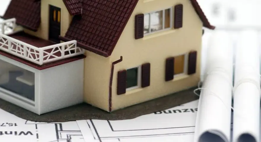 Modell eines Einfamilienhauses auf Bauplänen, daneben zwei aufgerollte Pläne. Ein Baukasten-BHKW könnte hier integriert werden.