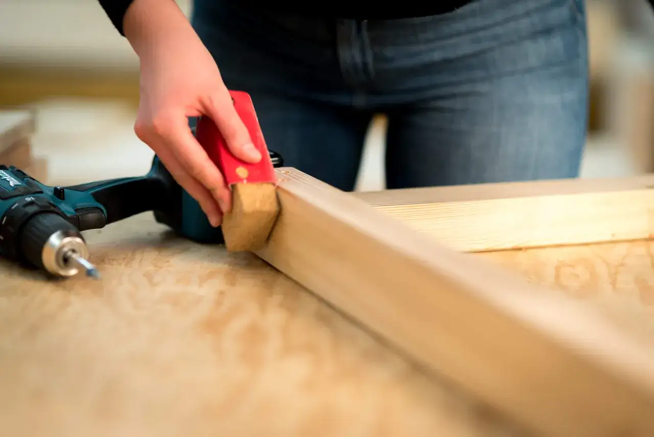 Person schleift Holz mit Schleifklotz und Akkuschrauber bereit. Perfekt vorbereitet, um das Holz zu versiegeln.