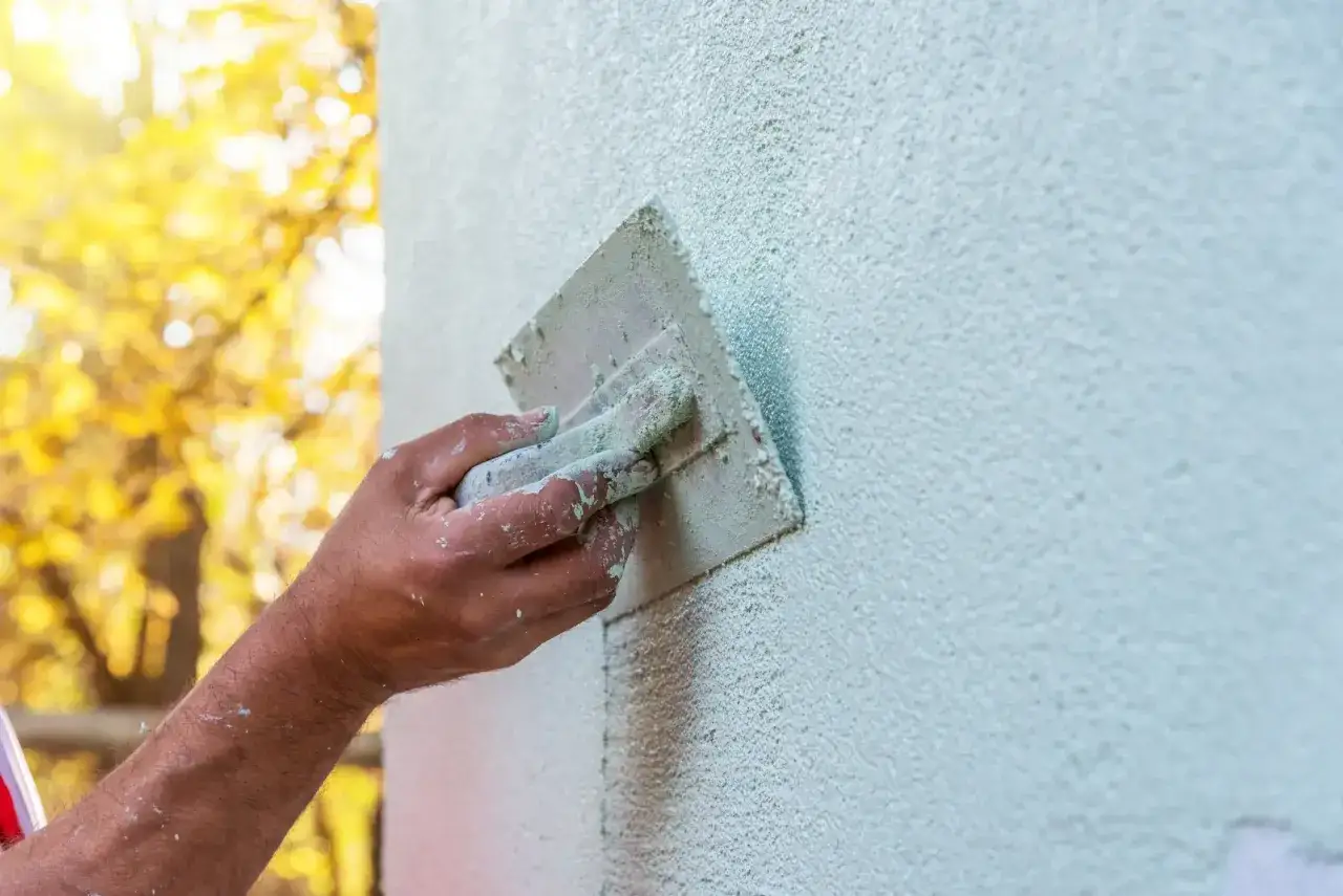 Hand glättet eine hellgrüne Wand mit einer Kelle. Die Textur des Innenputzes ist sichtbar. Die Kosten für Innenputz variieren je nach Material und Aufwand.