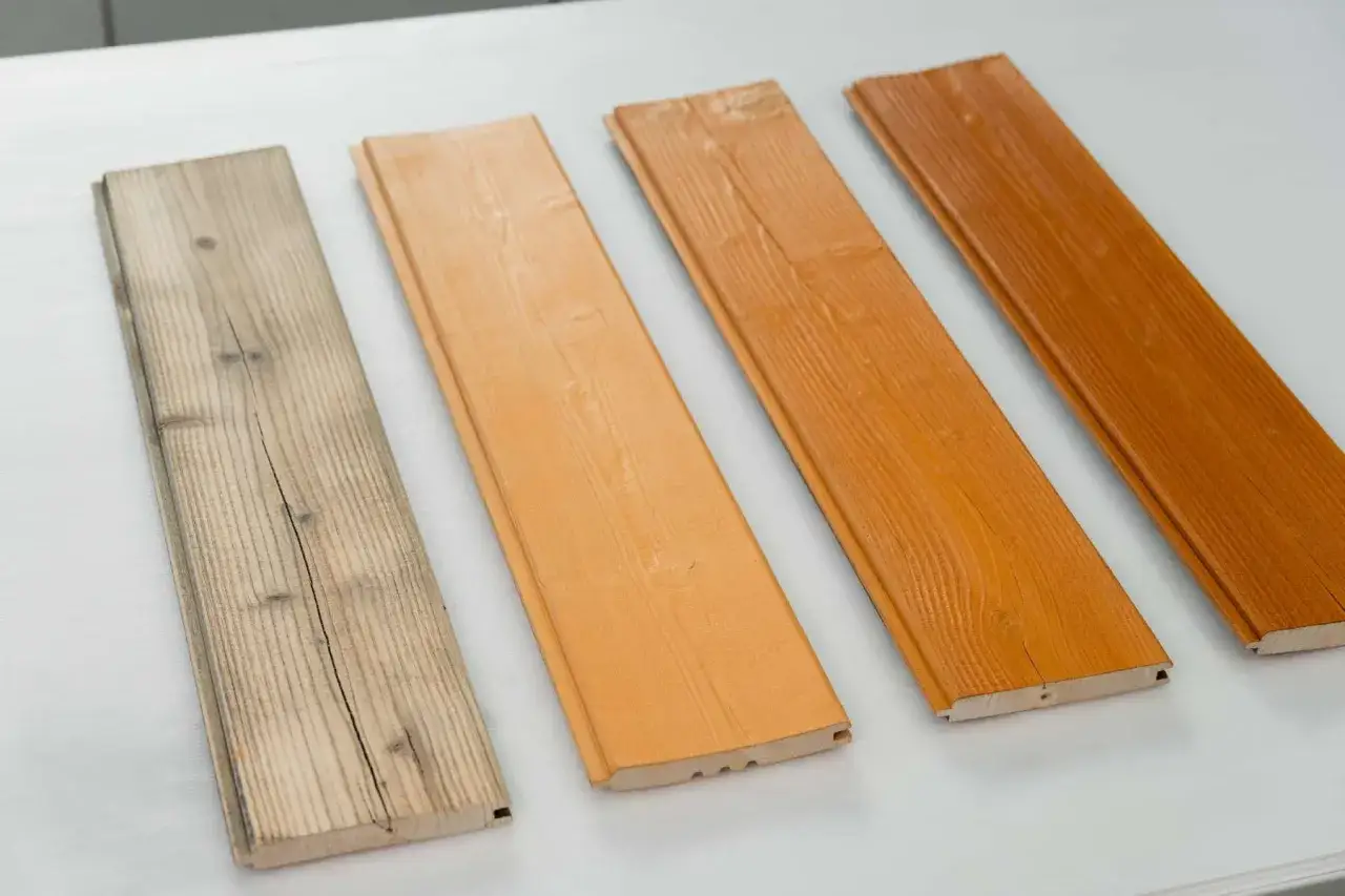 Vier Holzbretter nebeneinander, von links nach rechts: verwittertes Holz streichen, hellorange, orange und dunkelorange gestrichen.