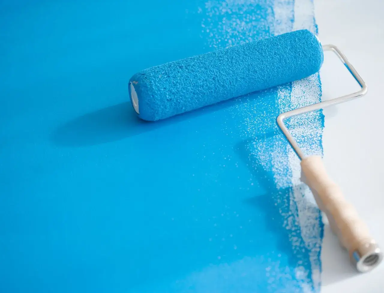 Ein blauer Farbroller streicht eine Wand. So einfach ist es, richtig streichen!