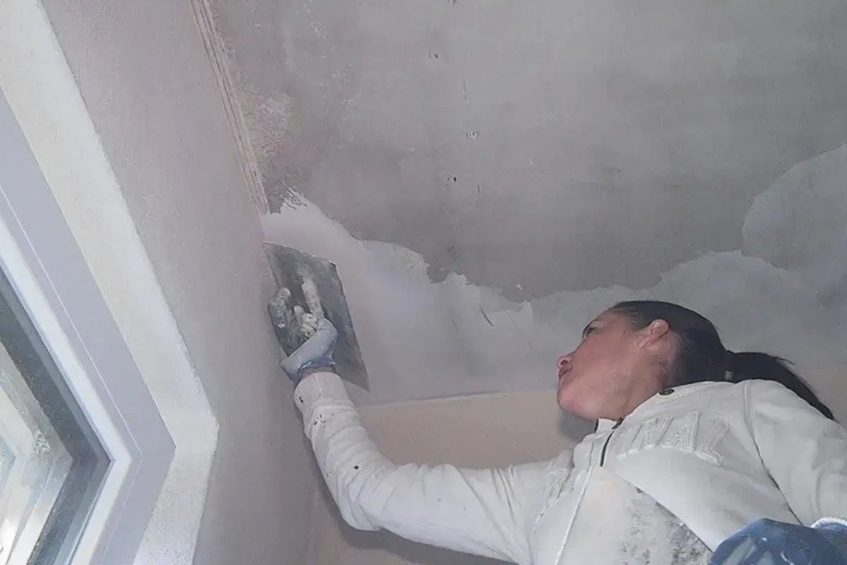 Frau spachtelt mit einem Werkzeug die Betondecke.