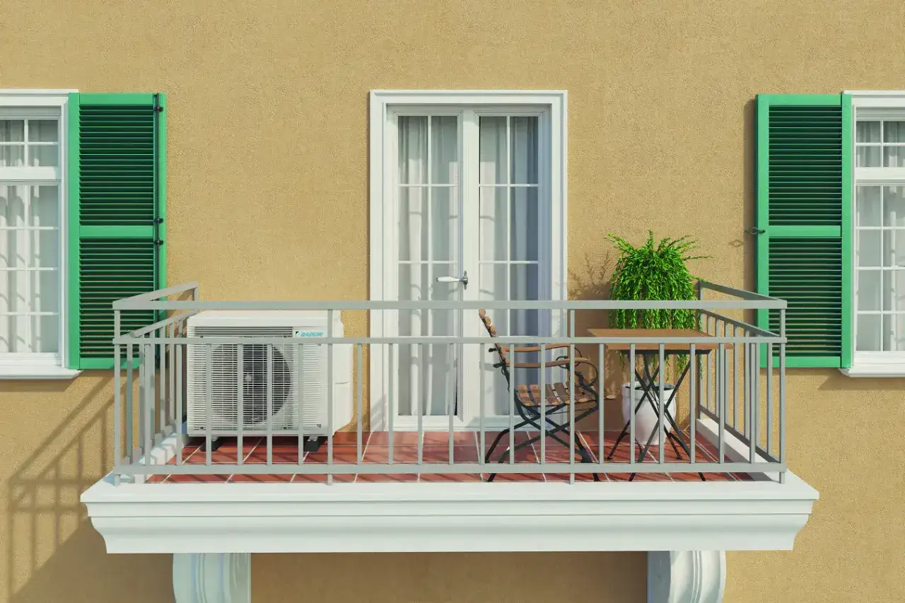 Balkon eines Mehrfamilienhauses mit Klimaanlage, Tisch und Stuhl. Gr&uuml;ne Fensterl&auml;den und eine T&uuml;r mit Vorh&auml;ngen.