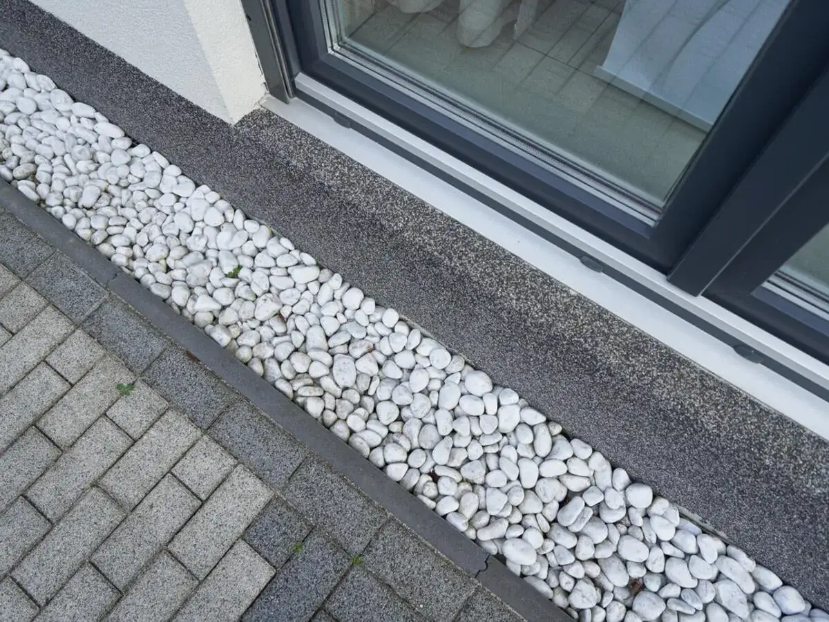 Weißer Kies als Spritzschutz am Haus schützt die Fassade und sieht gut aus.