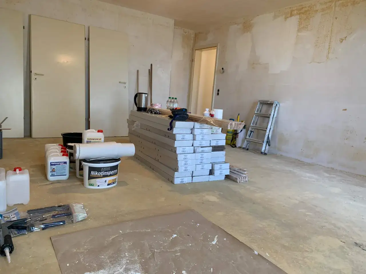 Materialien für die Renovierung einer Raucherwohnung: Tiefengrund, Nikotinsperre, Laminat, Pinsel und Leiter.