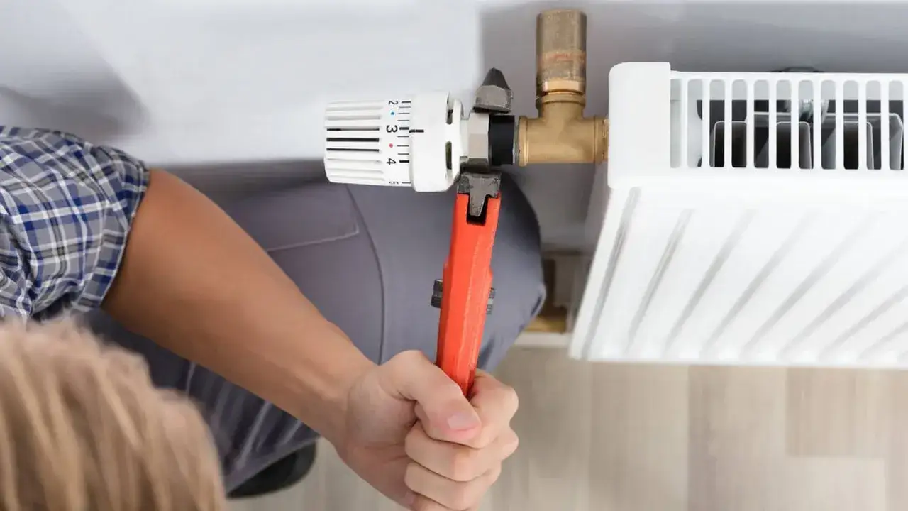 Hand mit Rohrzange dreht an einem Heizk&ouml;rperthermostat, um ein sehr altes Thermostat zu wechseln.